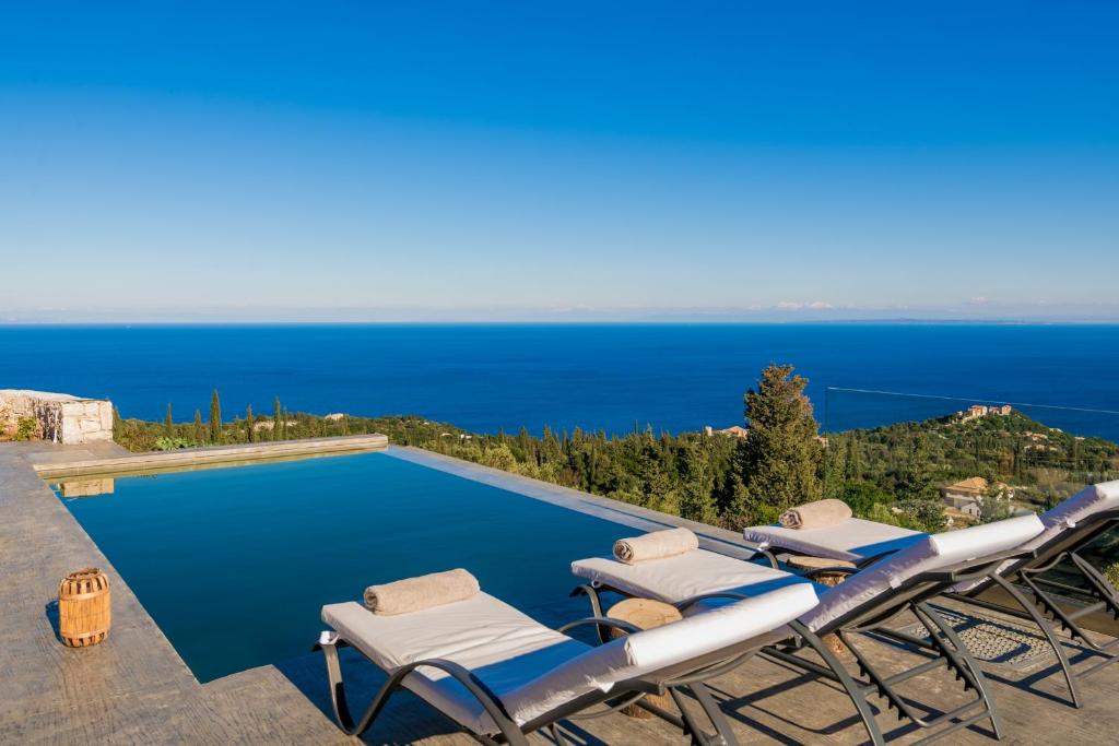 a pool with chairs and the ocean in the background at Nikolakos Villa in Agios Nikolaos