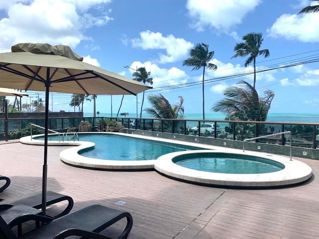 una piscina con sombrilla junto al océano en Hotel Ritz Condômino Adler Ricardo en Maceió