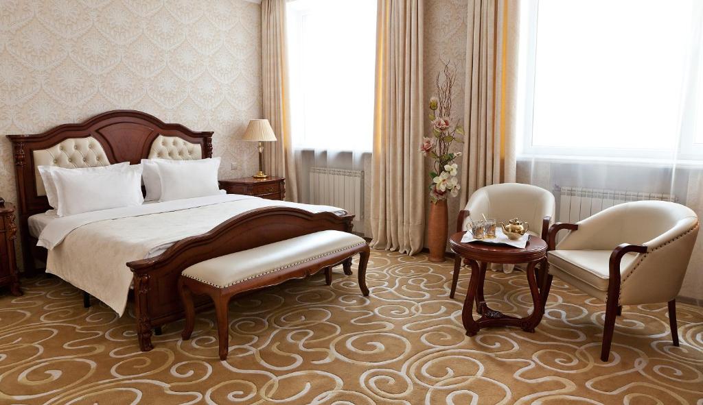 a bedroom with a bed and two chairs and a table at Grand Hall Hotel in Yekaterinburg