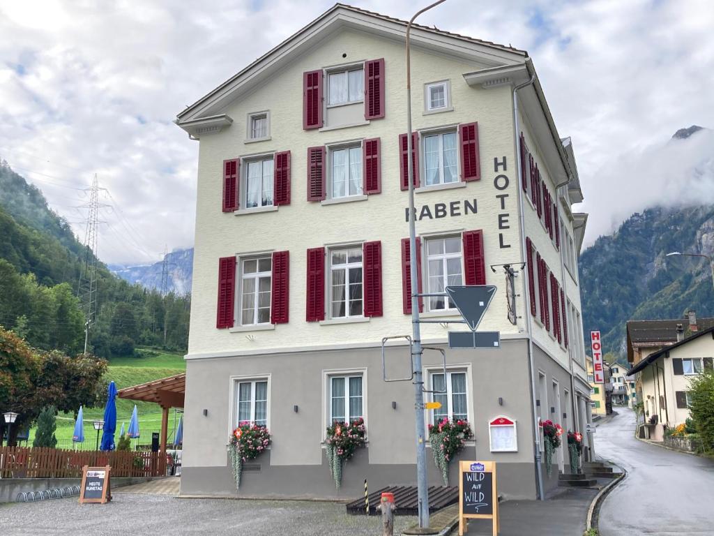 a white building with red shutters on a street at Hotel Restaurant Raben in Linthal