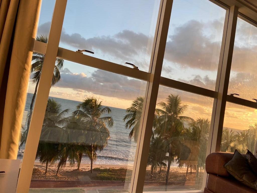 a window with a view of the ocean and palm trees at Flat vista Mar in João Pessoa