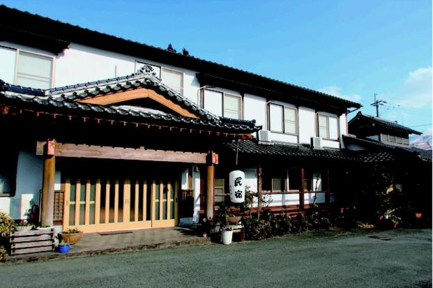 a building with an asian roof with a gate at Minshuku Asogen in Aso