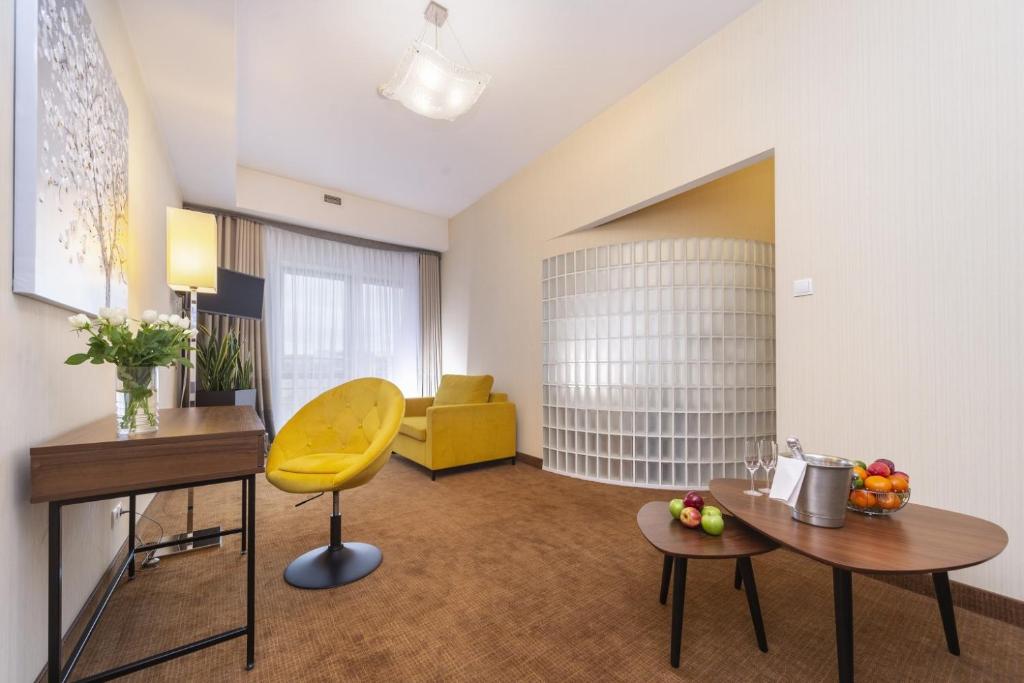 Bright sitting area featuring yellow armchair and sofa, wooden desk, glass-block partition and fruit-topped tables.