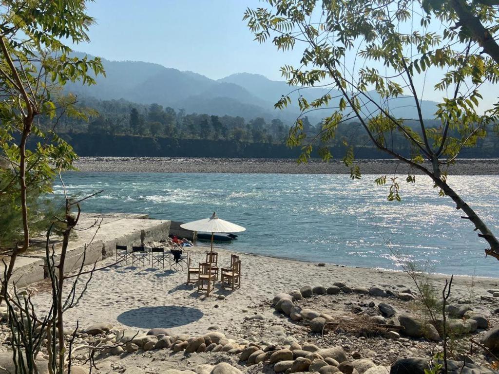 a beach with chairs and an umbrella and water at LUSHY DAYS BOOM CAMP in Tanakpur