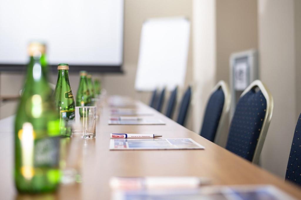 Shallow-focus view down conference table lined with bottles, glasses, pens and chairs.