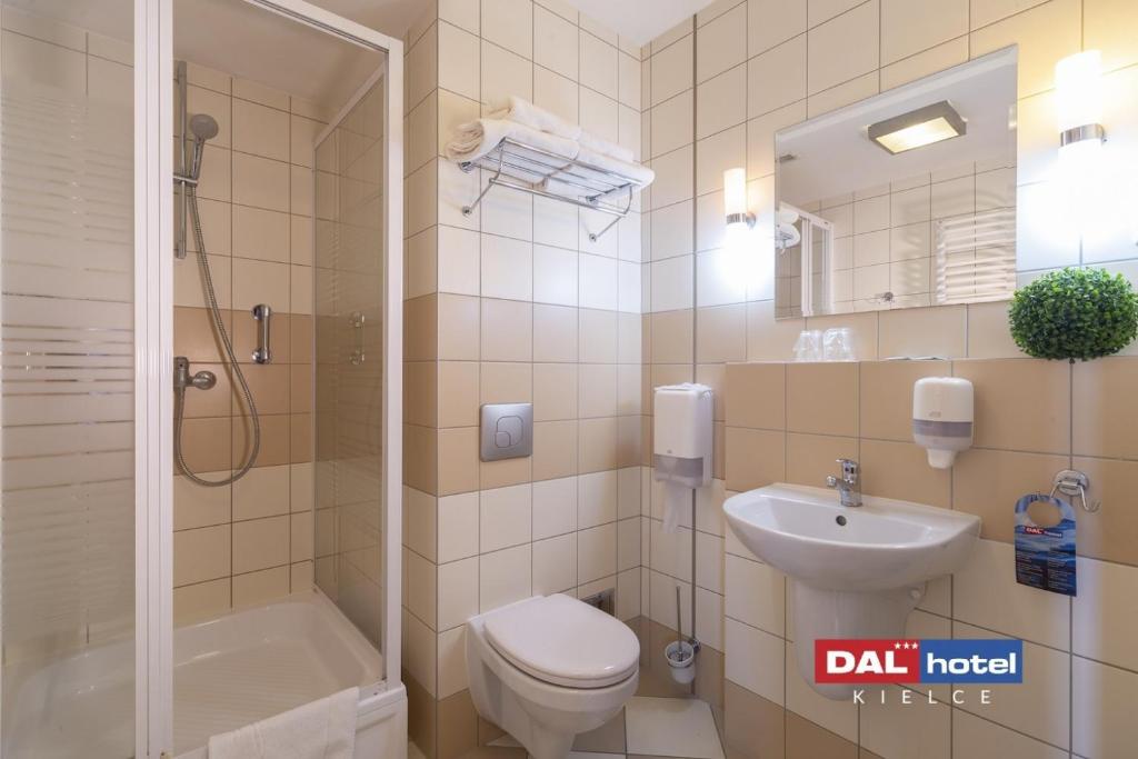 Compact tiled bathroom with glass shower, wall-mounted sink, toilet and folded towels, clean neutral tones