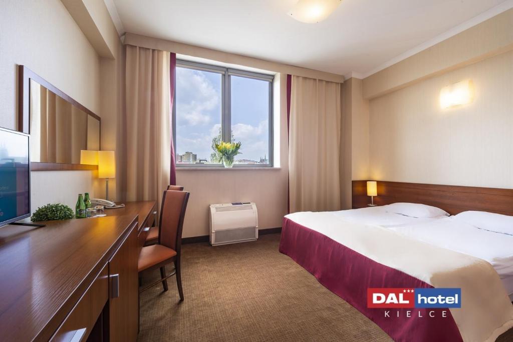 Comfortable double room with queen bed, wooden desk, window with flowers and neutral warm décor.