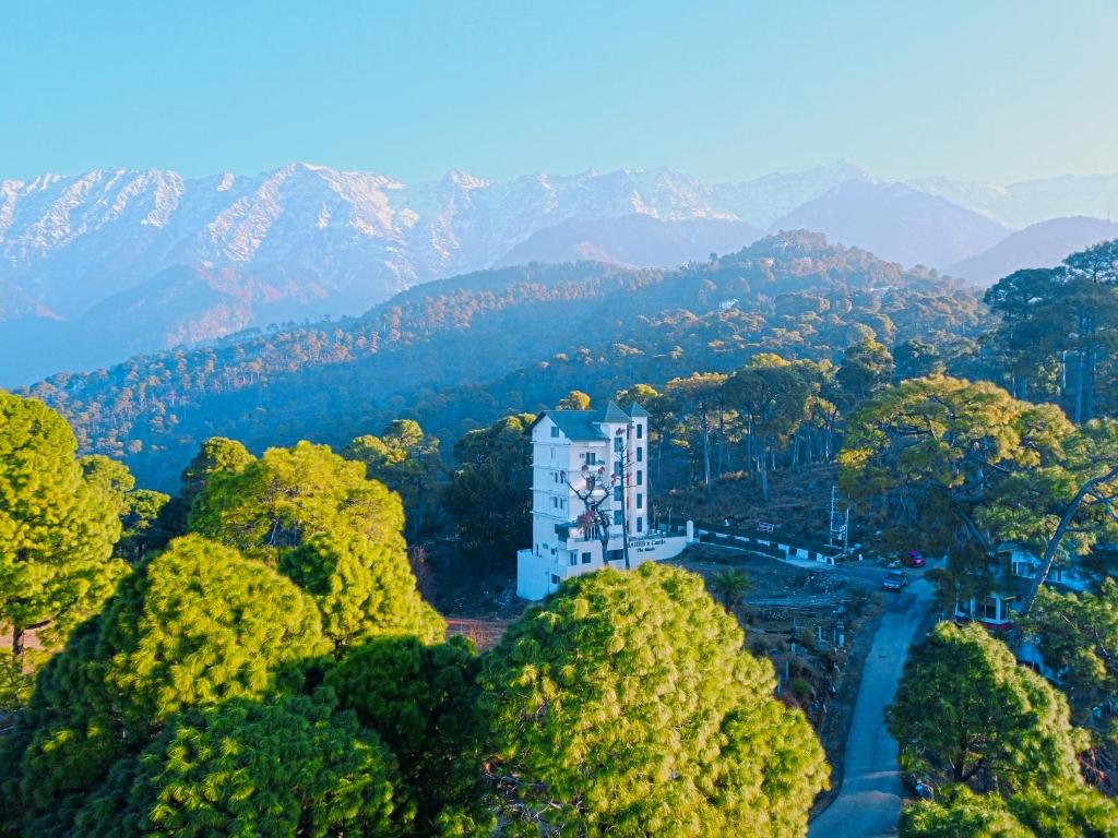 a building in the middle of a forest with mountains at Hotel Saheb's Castle McLeodganj in McLeod Ganj