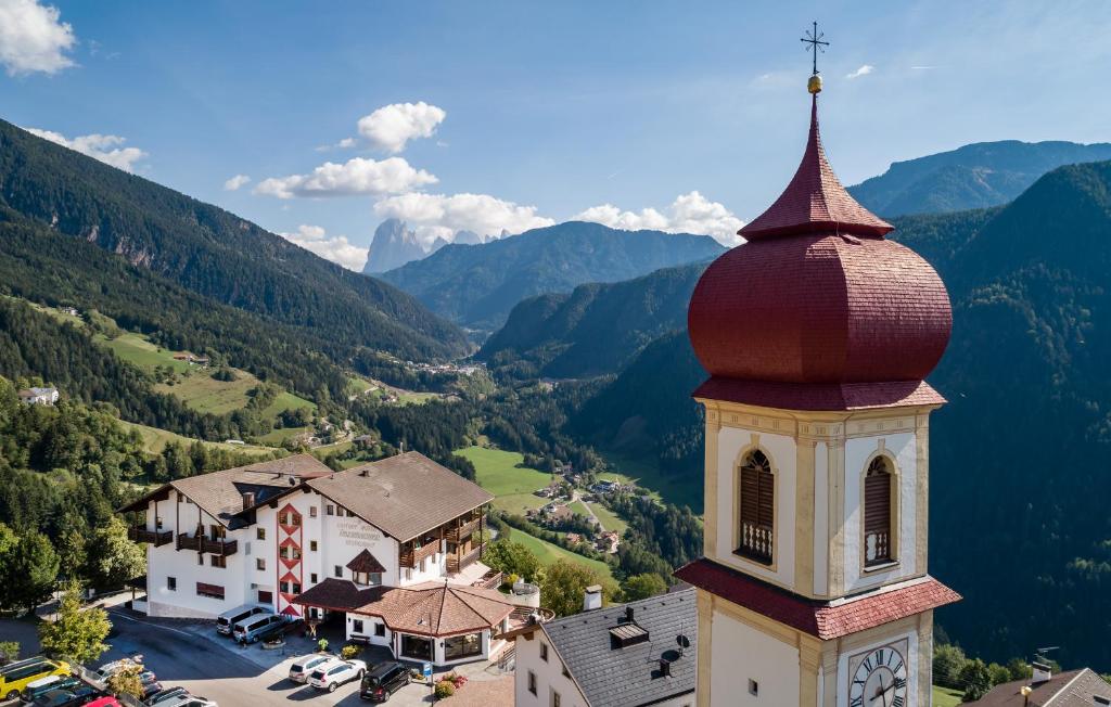 ein Gebäude mit einem Uhrturm mit Bergen im Hintergrund in der Unterkunft Hotel Überbacher in Lajen