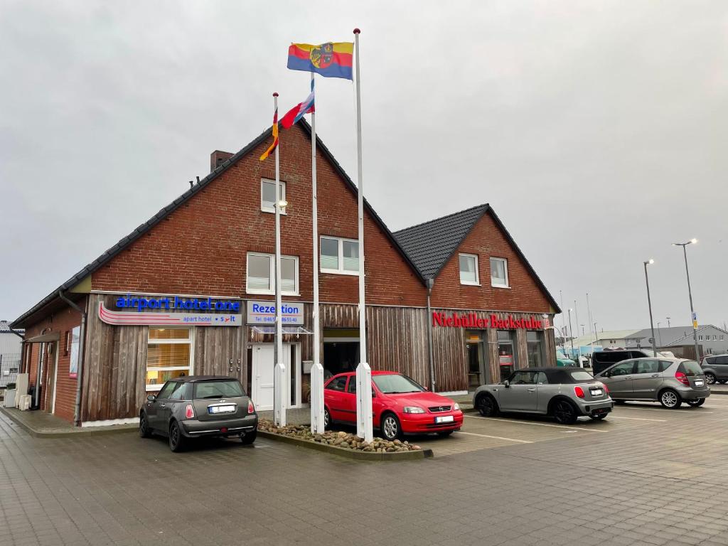 a building with a flag and cars parked in a parking lot at Airport Hotel One Aparthotel Sylt in Tinnum