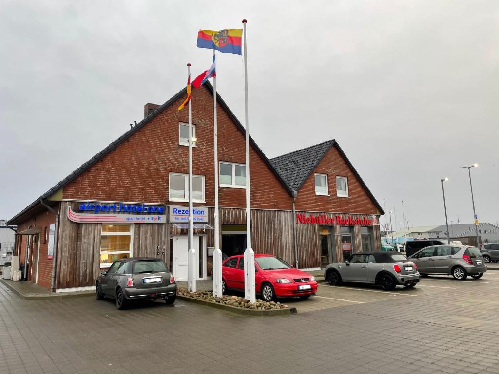 um edifício com uma bandeira e carros estacionados num parque de estacionamento em Airport Hotel One Aparthotel Sylt em Tinnum