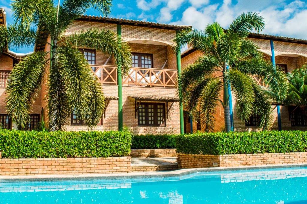 una casa con palmeras frente a una piscina en Hotel Vento Brasil en Paracuru