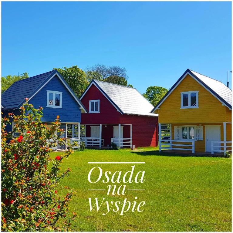 three houses in a yard with a sign in the grass at OSADA NA WYSPIE in Gdańsk