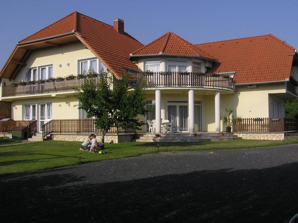 a child sitting in the grass in front of a house at Szalóky Apartmanház in Gyenesdiás