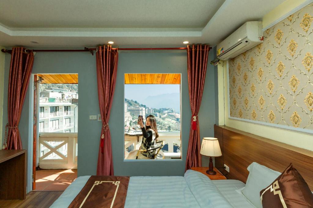 ein Schlafzimmer mit einem Fenster, in dem eine Frau ein Foto macht in der Unterkunft Sapa Unique Hotel in Sa Pa