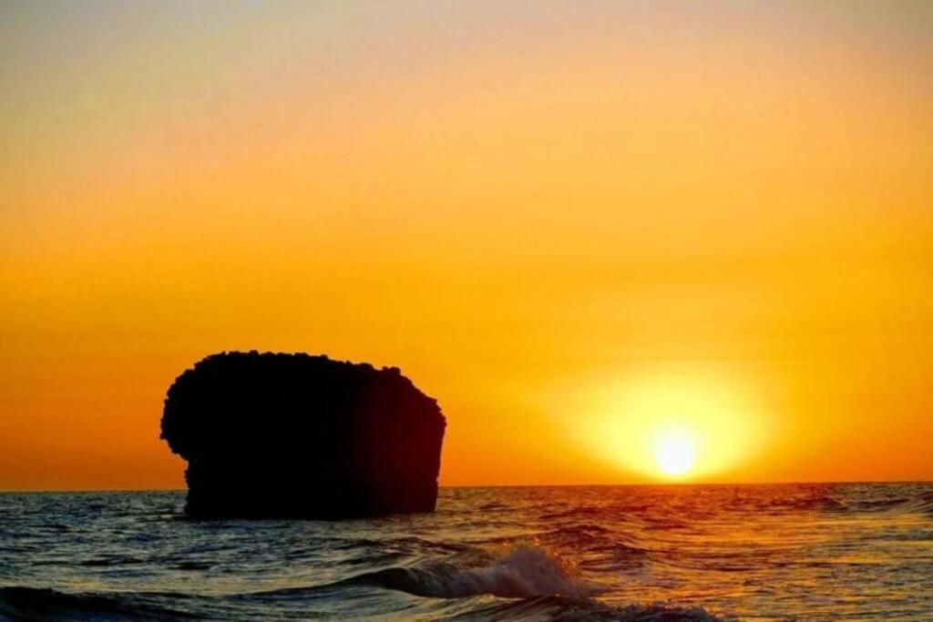 una puesta de sol sobre el océano con una roca en el agua en playa y naturaleza, en Matalascañas