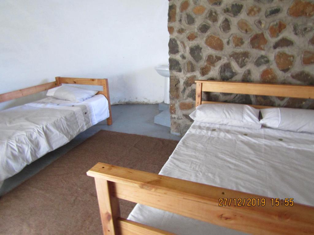 two beds in a room with a stone wall at Libibing chalets in Mokhotlong