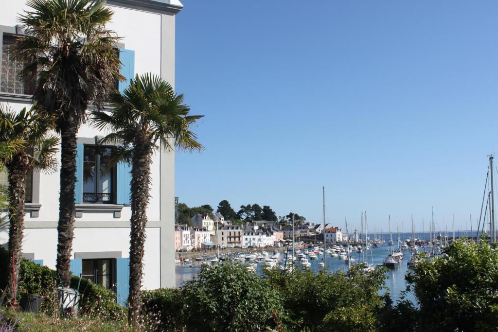 un bâtiment avec des palmiers en face d'un port de plaisance dans l'établissement Villa Pen Prad, à Sauzon