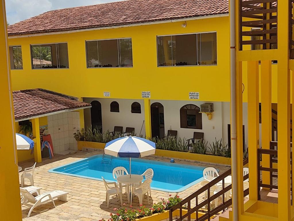 uma casa amarela com uma piscina e uma mesa com um guarda-chuva em Praia Sol Pousada em Prado