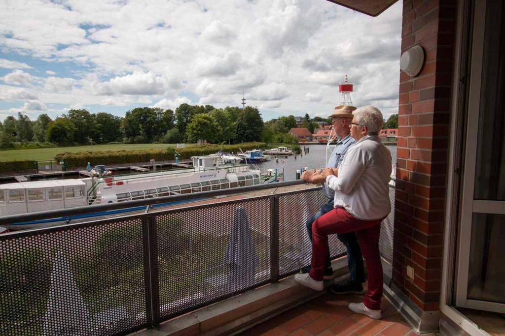 a man and woman sitting on a balcony overlooking a river at Hafen-Apartment Aurich in Aurich