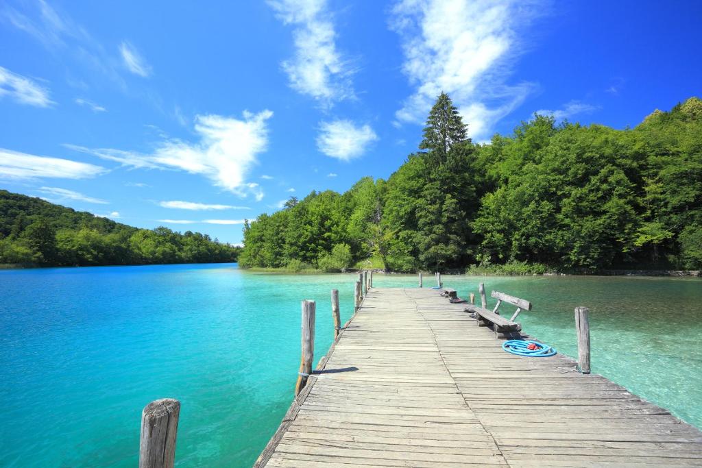 a dock on a lake with trees and blue sky at VIP Apartments & Room in Rakovica