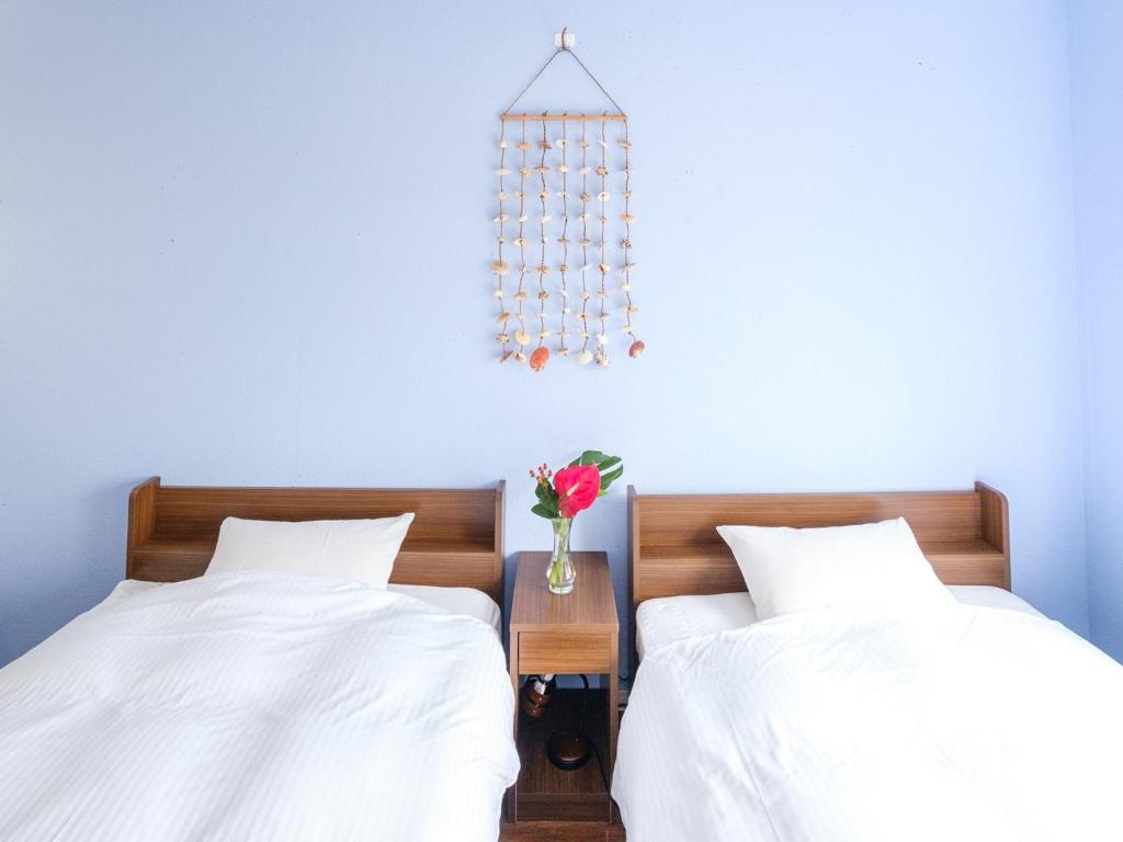 2 Betten mit weißer Bettwäsche und einer Vase aus Blumen in der Unterkunft Hotel Shion no Umi - Vacation STAY 98886 in Miyako-jima