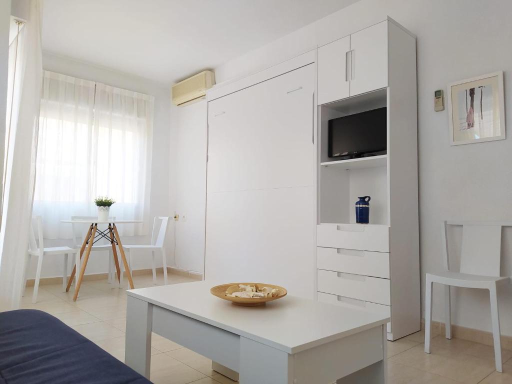 a white living room with a table and a tv at Apartamentos Pagán in Santiago de la Ribera