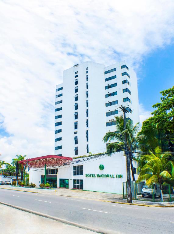 a white building with a palm tree in front of it at Hotel Nacional Inn Recife Aeroporto in Recife