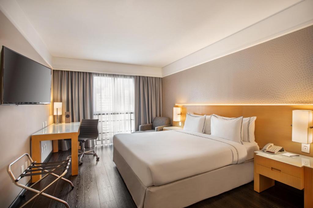 Una habitación de hotel con una cama grande y un escritorio. en Meliá Campinas, en Campinas