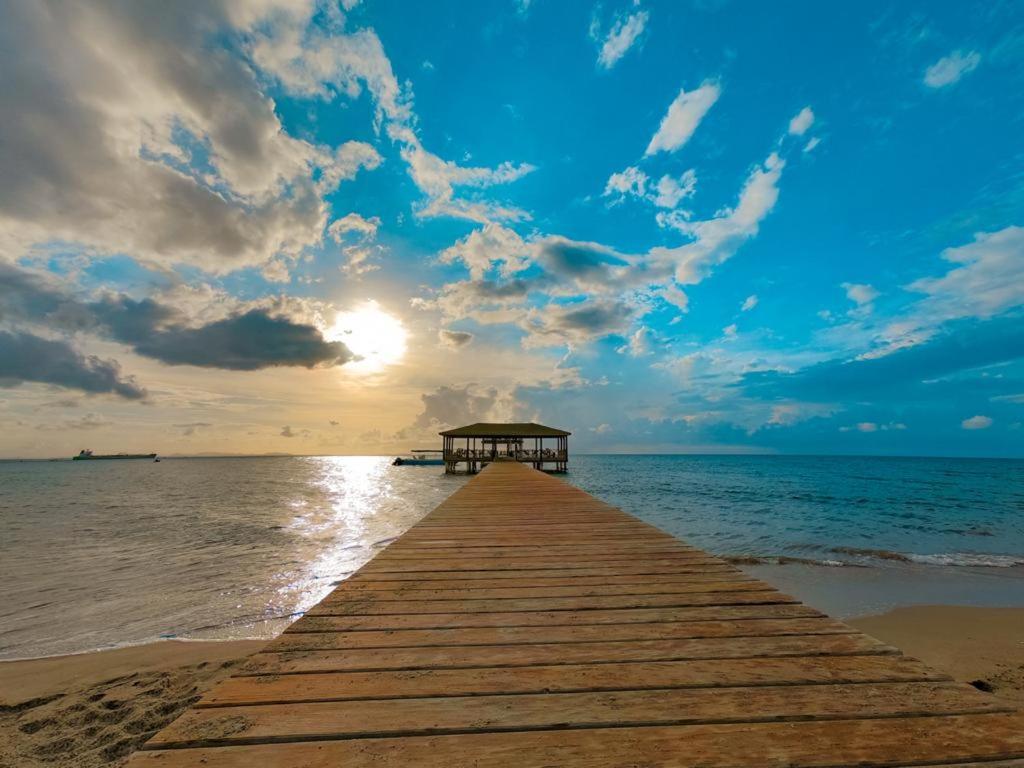 a wooden pier stretches out into the ocean with the sun at La Ensenada Beach Resort in Tela