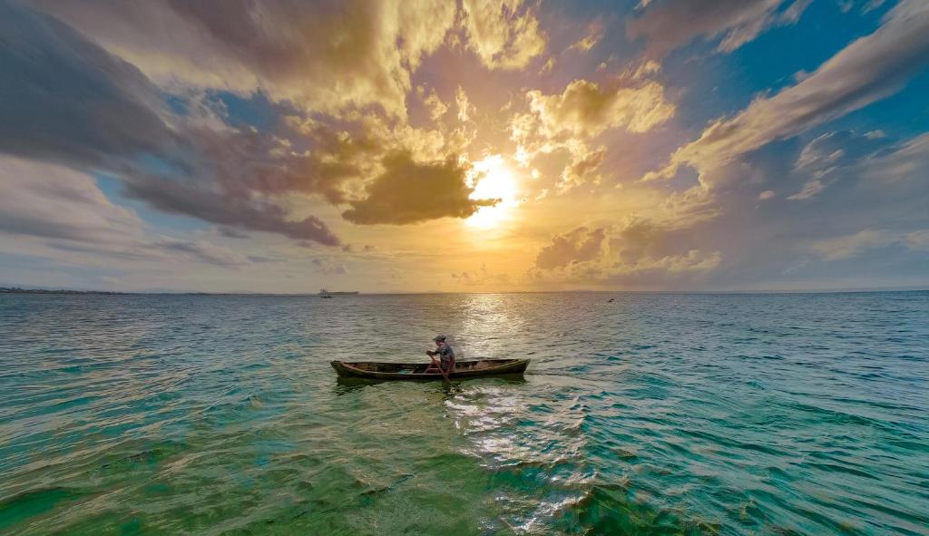 a man in a boat in the ocean at sunset at La Ensenada Beach Resort in Tela