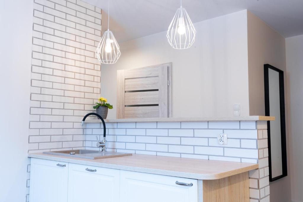 a white kitchen with a sink and two lights at Apartament Konopnickiej10 in Gdańsk