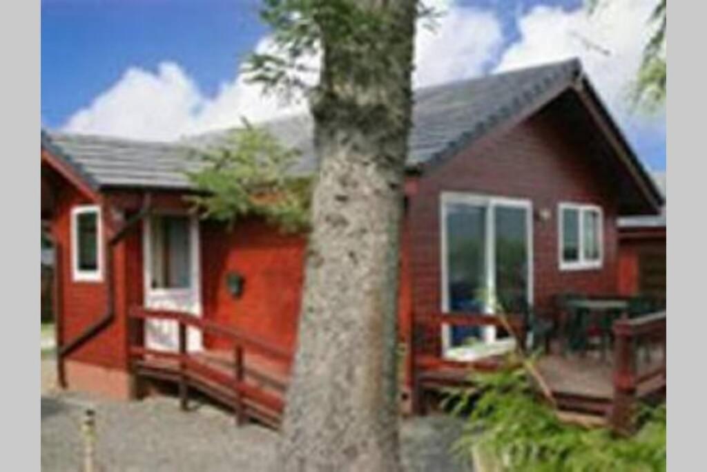 a red house with a porch and a tree at Heron Lodge, edge of Mabie Forest Dumfries in Dumfries