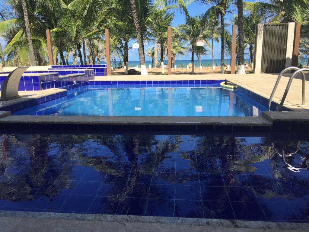 a swimming pool with palm trees and the ocean at Suspiro da Bahia Pé na areia in Salvador