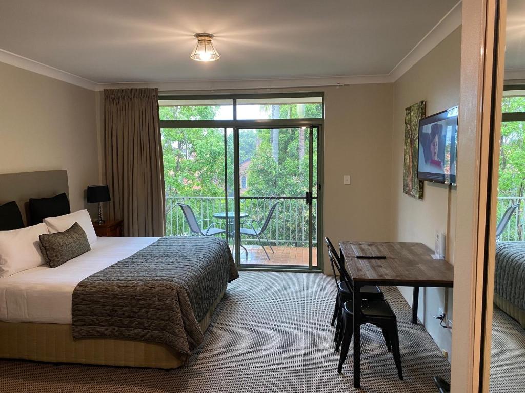 1 dormitorio con cama, escritorio y balcón en The Belmore Apartments Hotel en Wollongong
