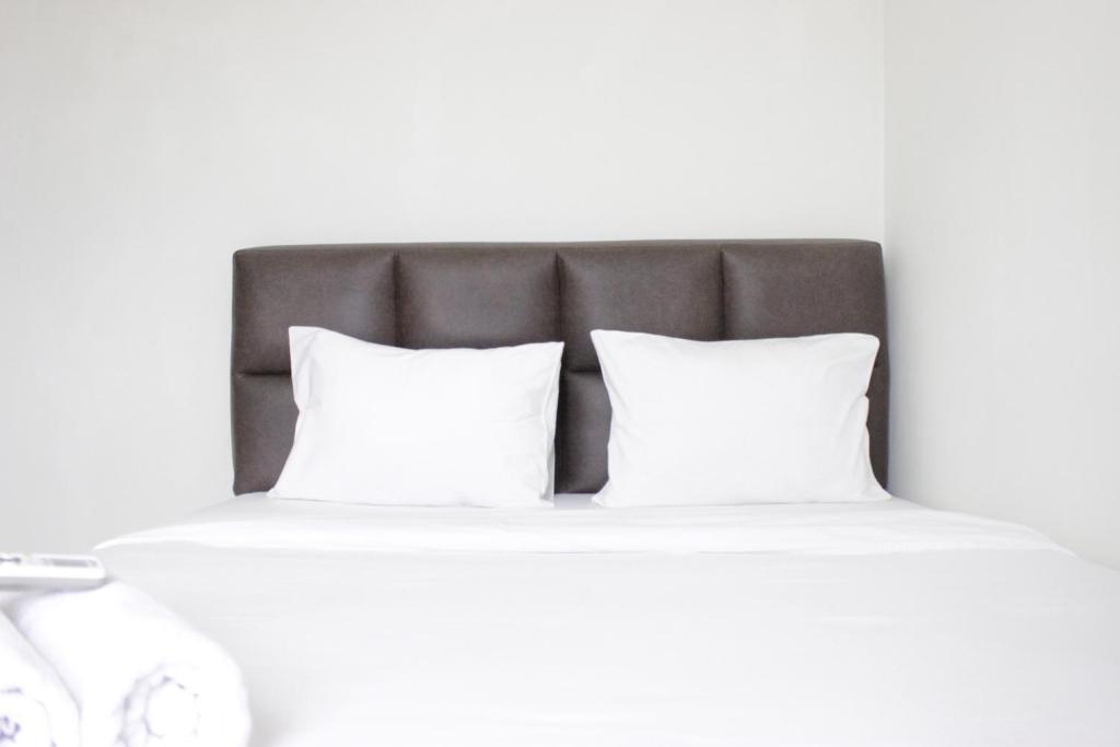 un letto con due cuscini bianchi e una testiera grigia di Homey 2BR Majesty Apartment near Maranatha University By Travelio a Bandung