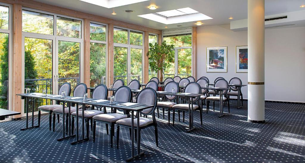 eine Reihe von Tischen und Stühlen in einem Zimmer mit Fenstern in der Unterkunft Victor's Residenz-Hotel Saarbrücken in Saarbrücken