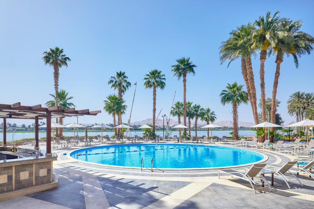 a pool at the resort with palm trees and chairs at Steigenberger Resort Achti in Luxor
