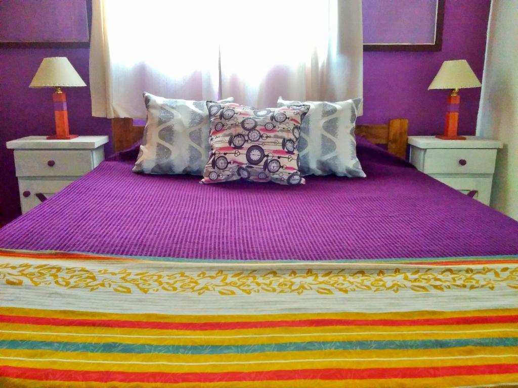 Una cama con sábanas y almohadas moradas en un dormitorio. en Palmares al cerro en Capilla del Monte