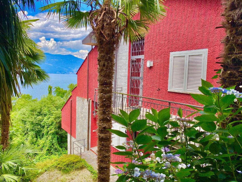 un bâtiment rouge avec un palmier devant lui dans l'établissement Appartamento Buresso, à Porto Valtravaglia