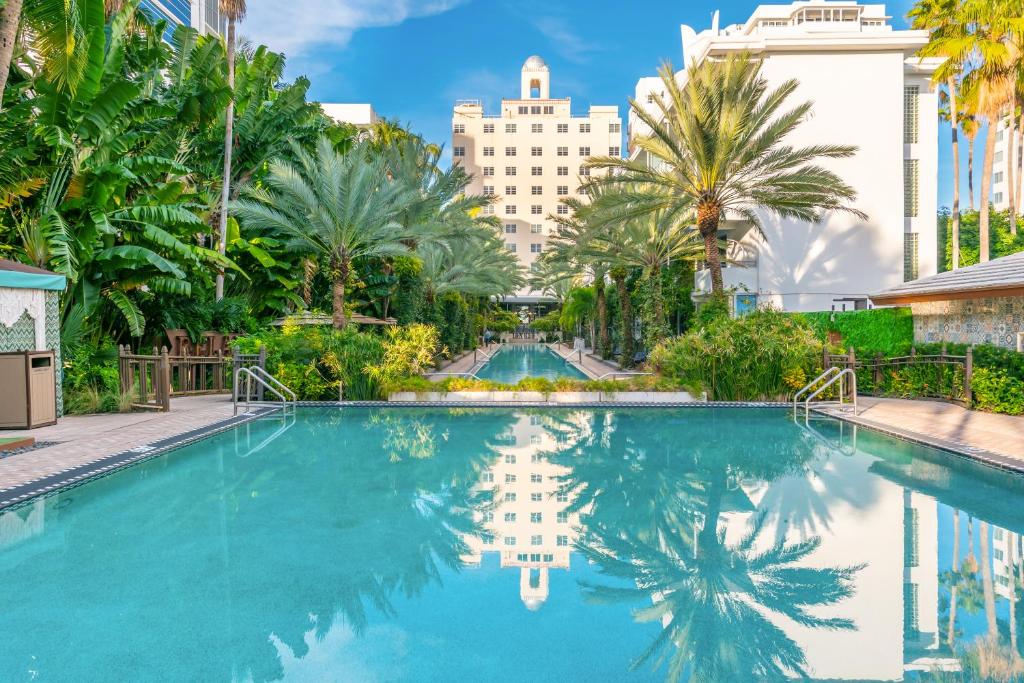 a swimming pool with palm trees and buildings in the background at National Hotel, An Adult Only Oceanfront Resort in Miami Beach