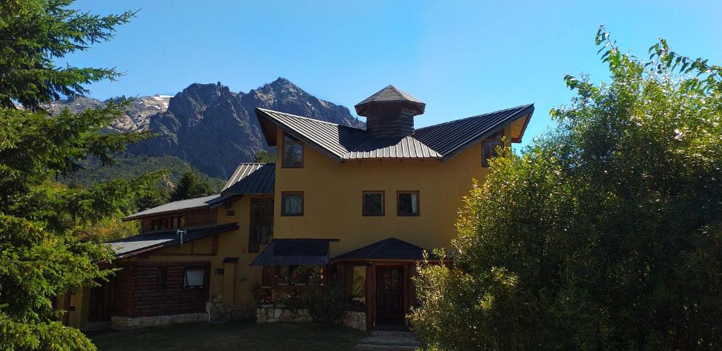 a large yellow house with a roof with mountains in the background at Ailín Maiá Apartamentos Casa de Montaña in San Carlos de Bariloche