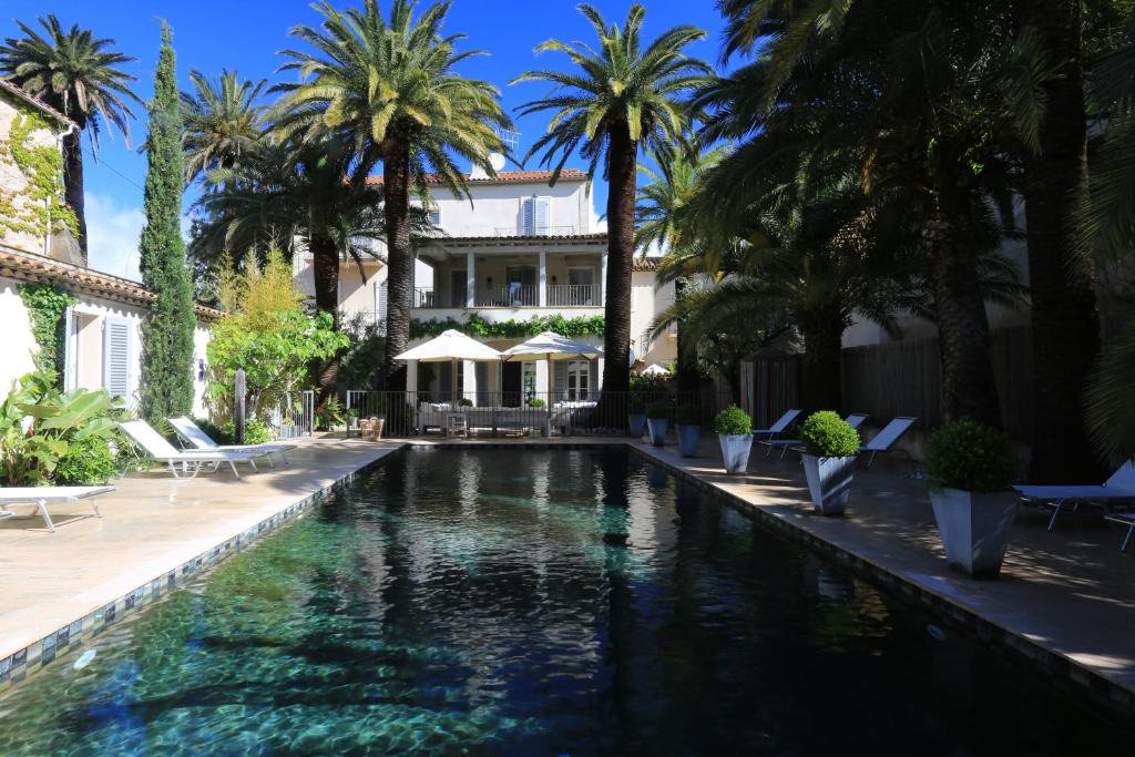 a swimming pool in front of a house with palm trees at Pastis Hotel St Tropez in Saint-Tropez