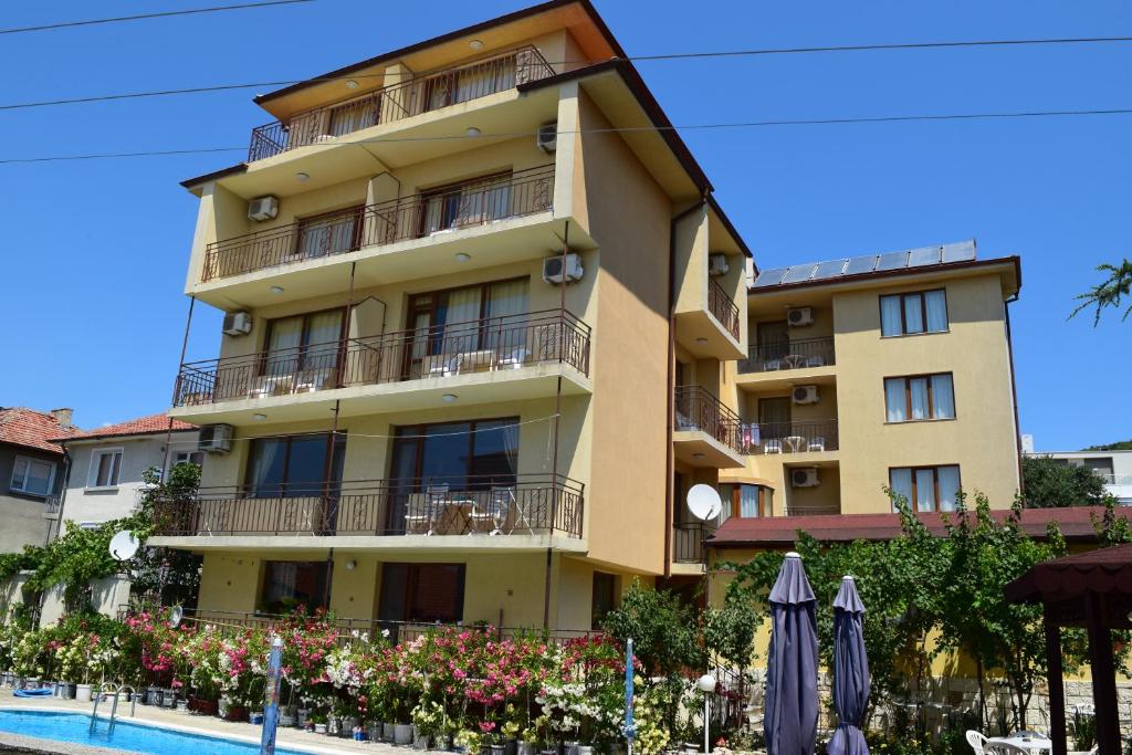 a yellow apartment building with a swimming pool and umbrellas at Family Hotel Chris in Sveti Vlas
