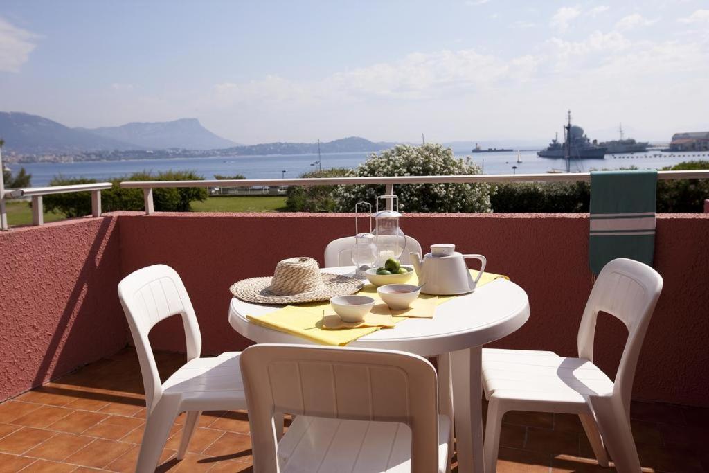 une table et des chaises blanches sur un balcon avec vue sur l'eau dans l'établissement Les jardins de la Côte d'azur, à Saint-Mandrier-sur-Mer