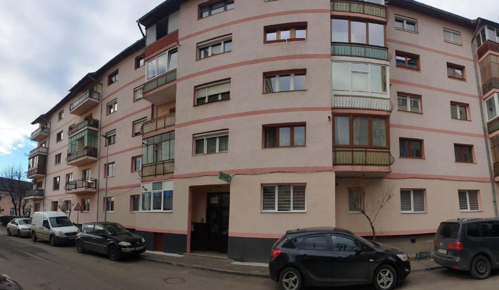 Un gran edificio rosa con coches aparcados delante. en Apartament Central Iulia, en Sibiu