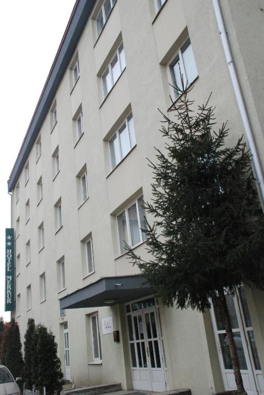 a large white building with a tree in front of it at Hotel Merkur in Miercurea-Ciuc
