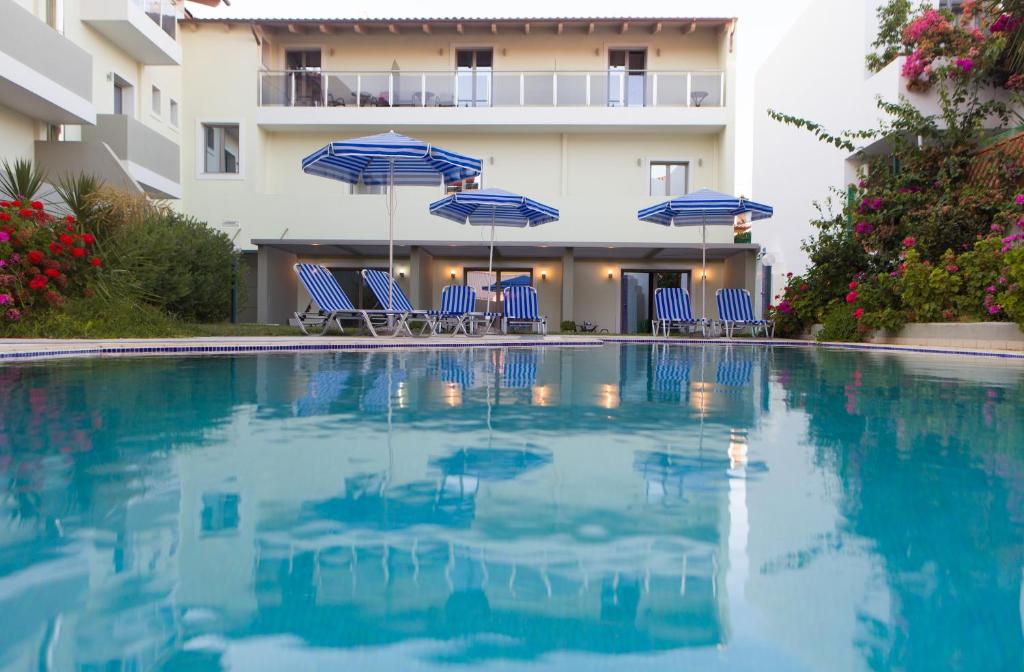 una piscina con sillas y sombrillas azules en Panormo Beach Hotel, en Panormos Rethymno