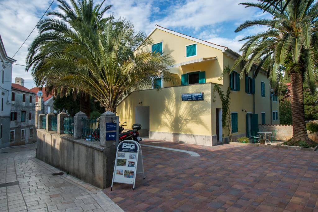 a yellow building with palm trees in front of it at BigBlue house Apartman Amelie in Veli Lošinj