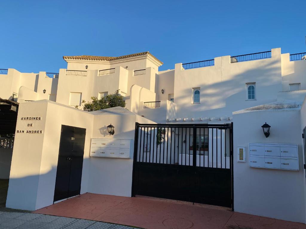 um edifício branco com um portão preto em frente em Precioso adosado rodeado de un entorno verde natural y muy cerca de la playa em Chiclana de la Frontera